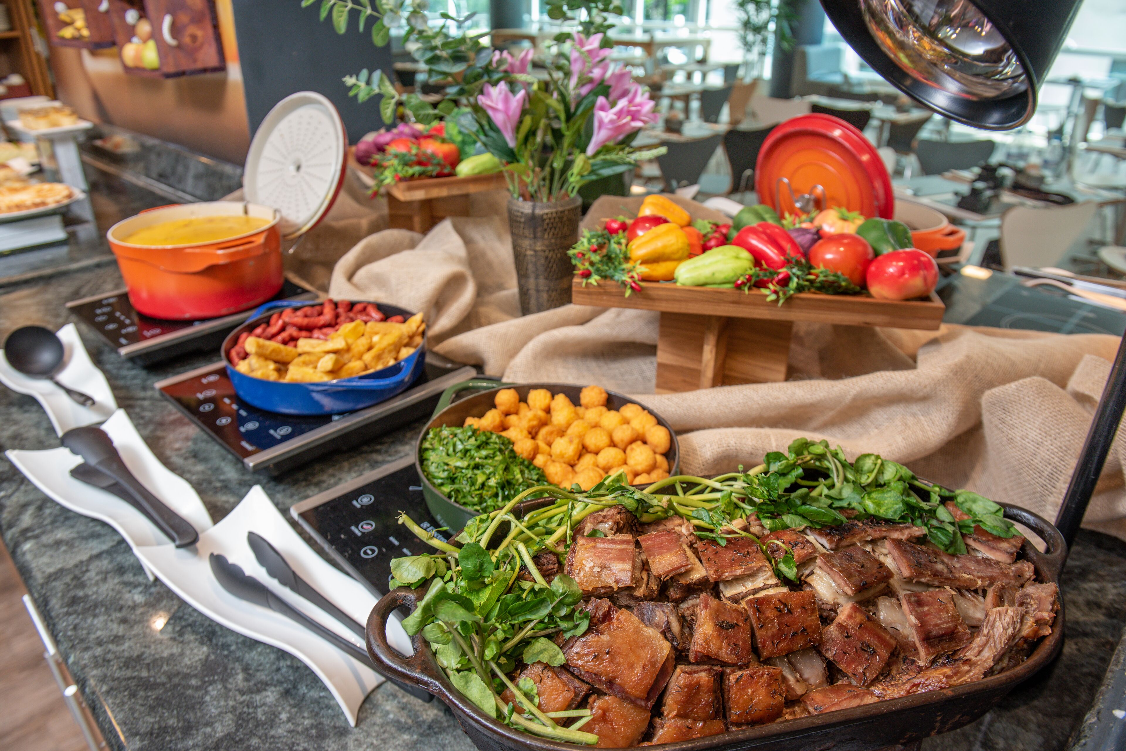 Un bufé con diversos platos, incluyendo carne, verduras y un bol de batatas cortadas en cubos.