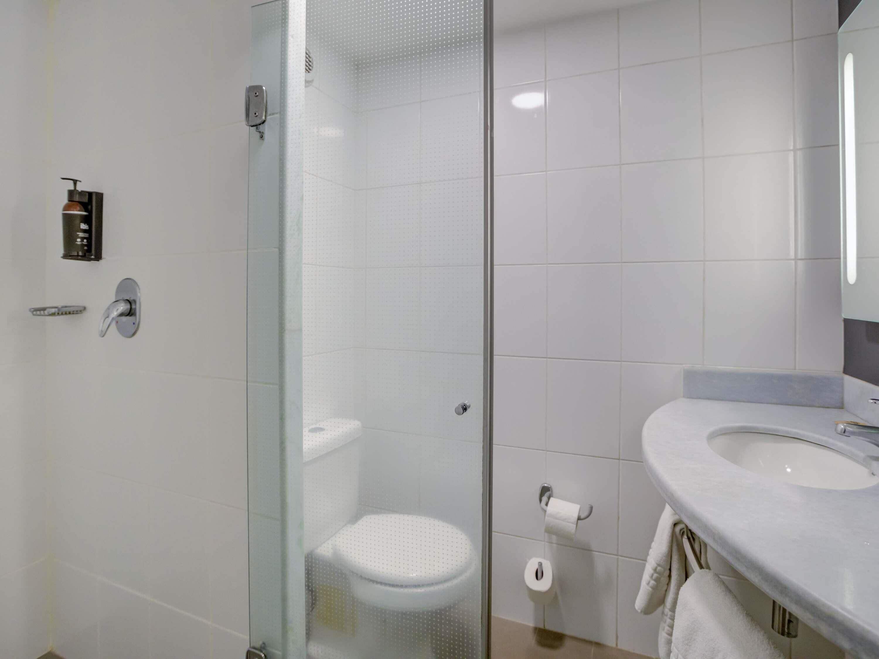 Une salle de bain moderne avec une douche à parois de verre, des toilettes blanches et un lavabo avec une serviette.
