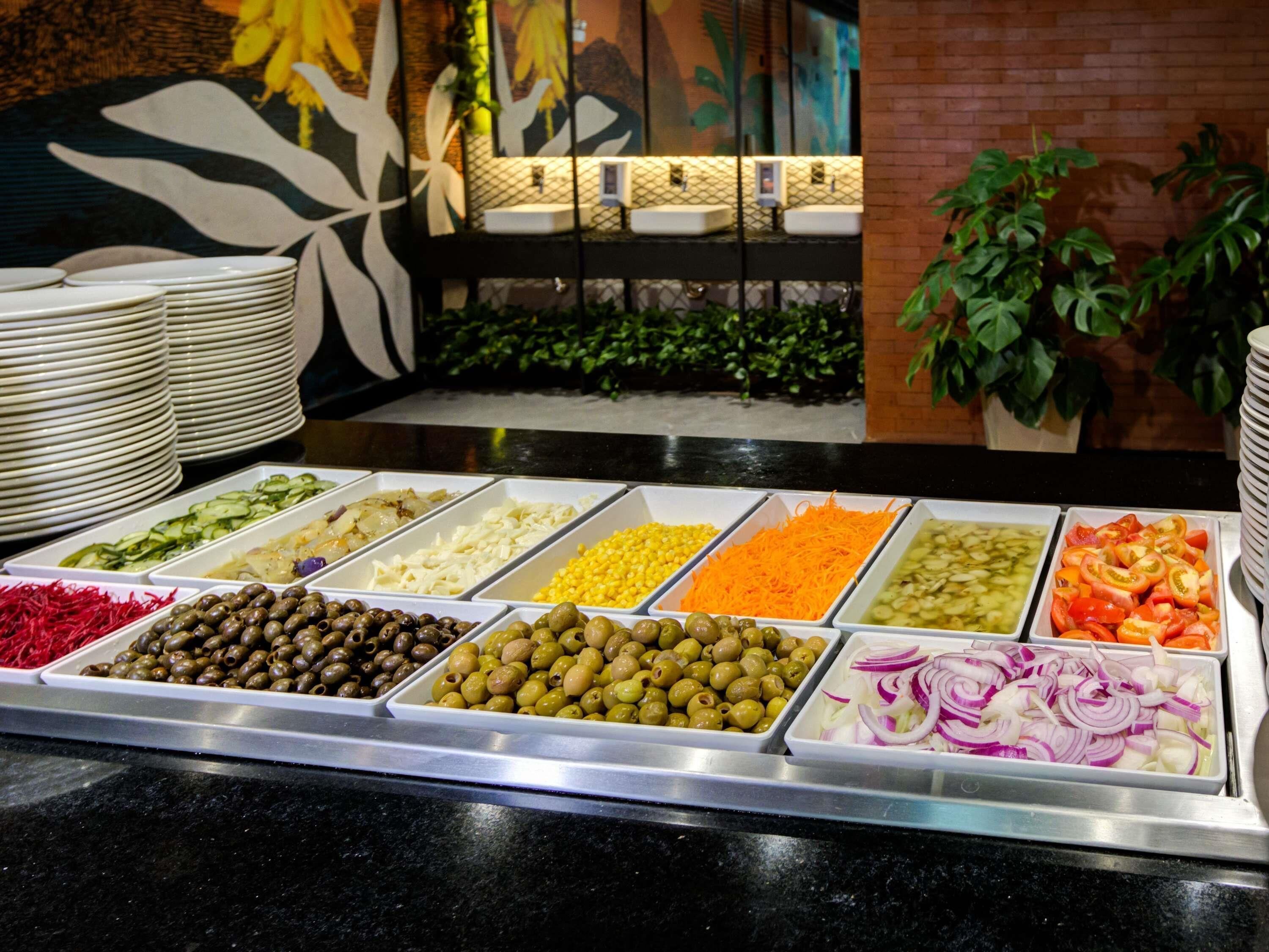 A buffet with various food options including olives, corn, carrots, and onions.