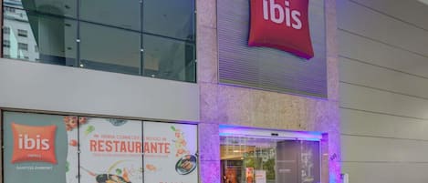 A modern building with a prominent 'ibis' sign above the entrance, large windows, and a digital display.