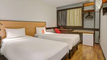 Habitación de hotel con dos camas, un escritorio, una silla, un refrigerador pequeño y un espejo.