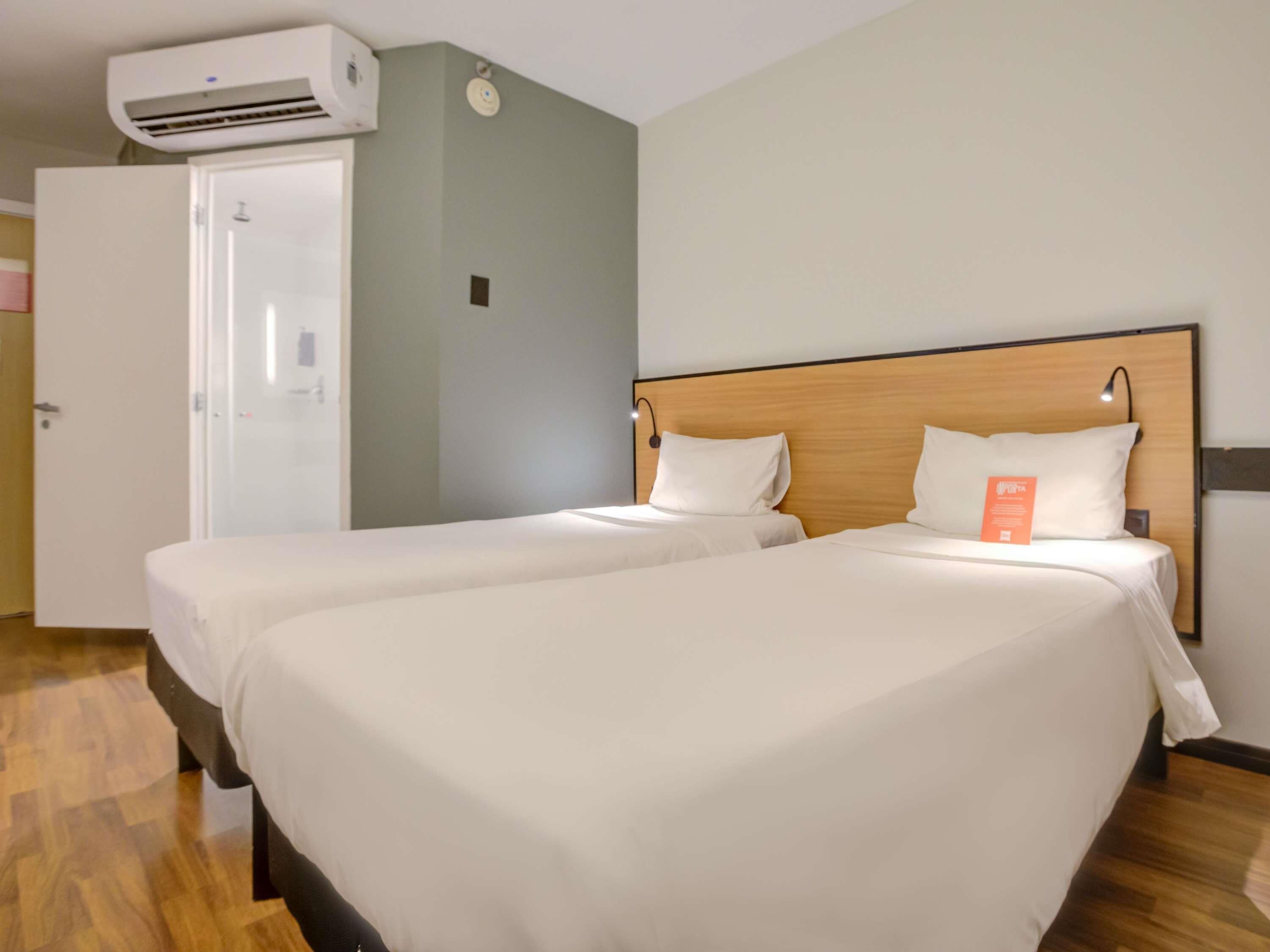 A hotel room with two beds, a wooden headboard, a white door, and an air conditioning unit.