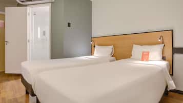 A hotel room with two beds, a wooden headboard, a white door, and an air conditioning unit.