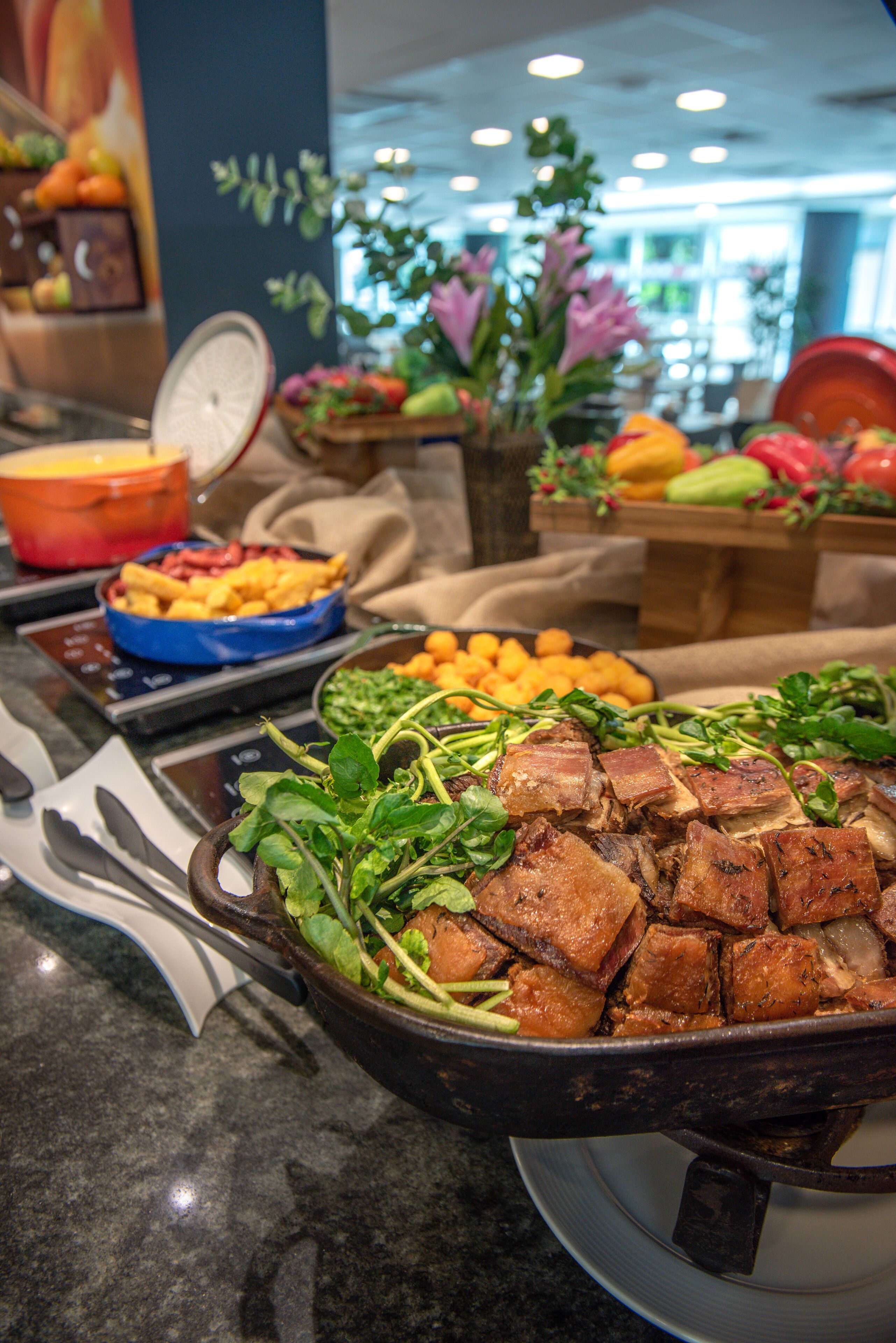 Buffet com diversos pratos, incluindo um grande prato de carne, saladas e uma tigela de frutas.