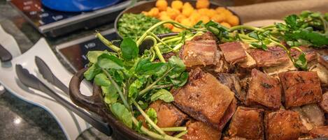 Un bufé con diversos platos, incluyendo una gran bandeja de carne, ensaladas y un bol de fruta.