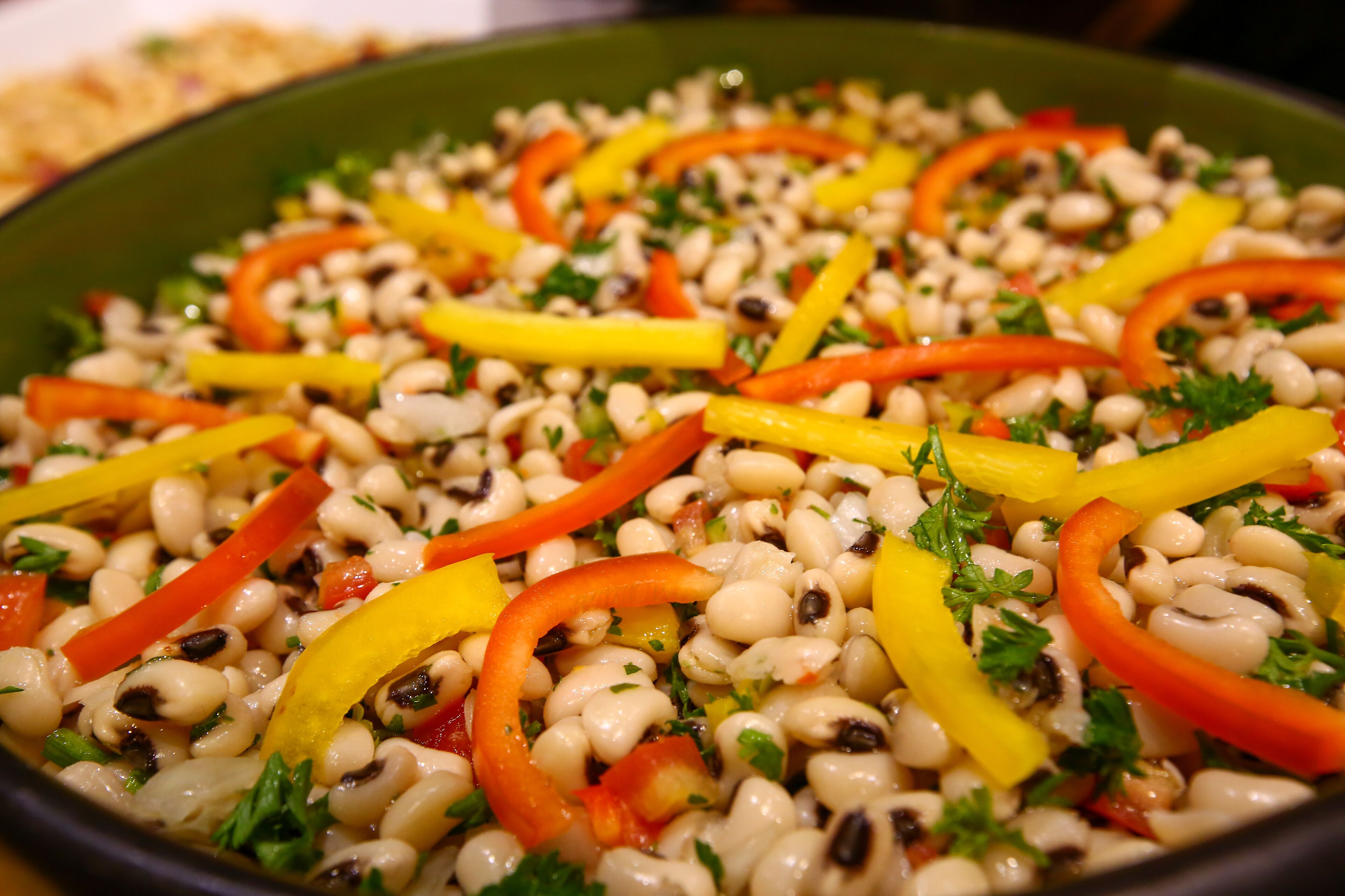 A close-up of a bean salad with red and yellow bell peppers and parsley.
