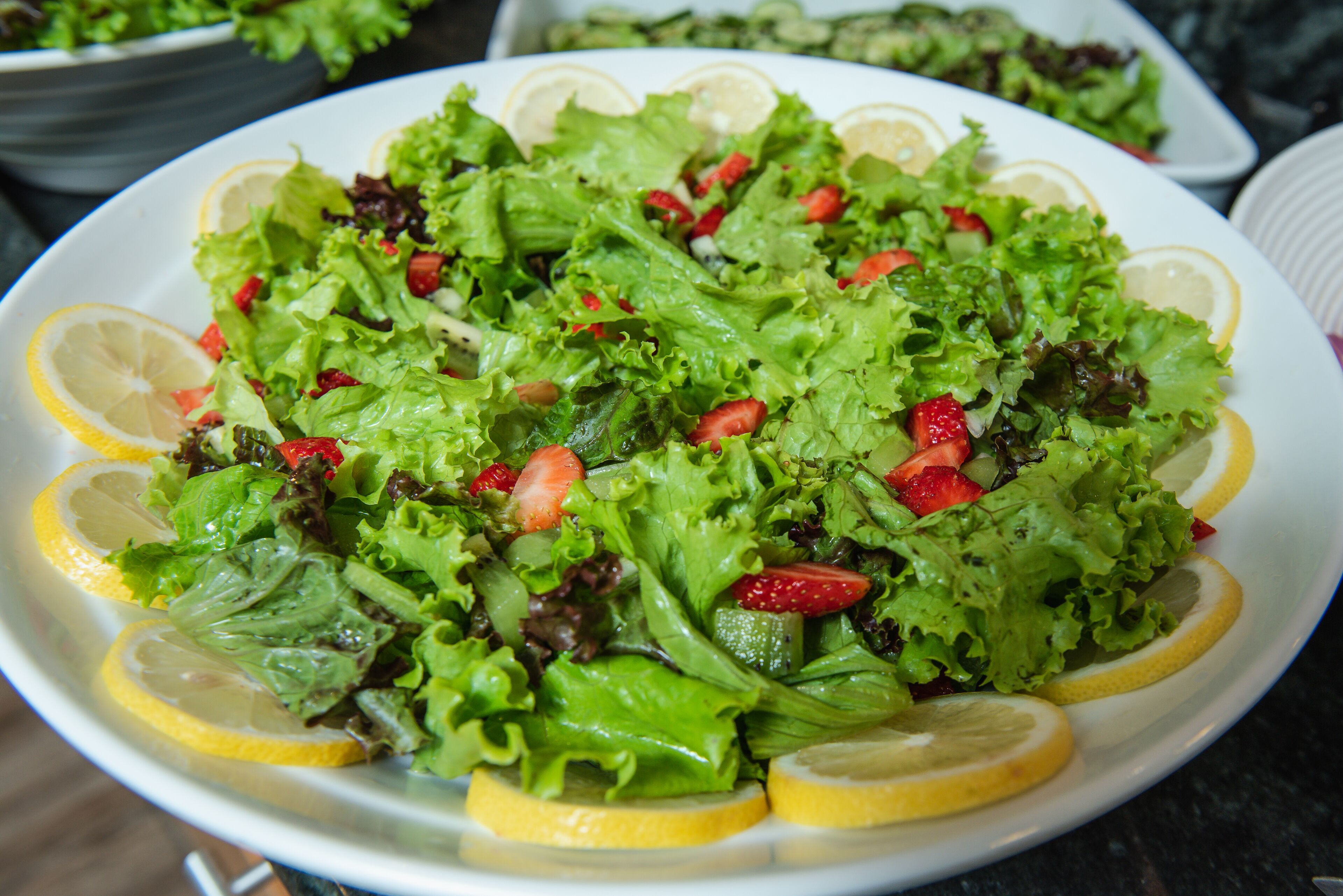 A plate of salad with lettuce, strawberries, and lemon slices.