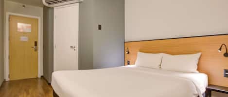 A hotel room with a large bed, an air conditioning unit, a wooden headboard, and a nightstand.