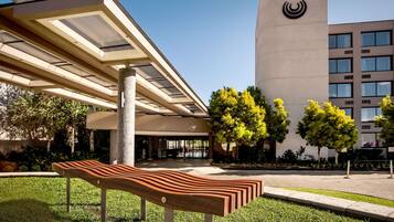 Um edifício moderno com um logotipo marcante, uma área de estar coberta ao ar livre e um gramado bem cuidado.