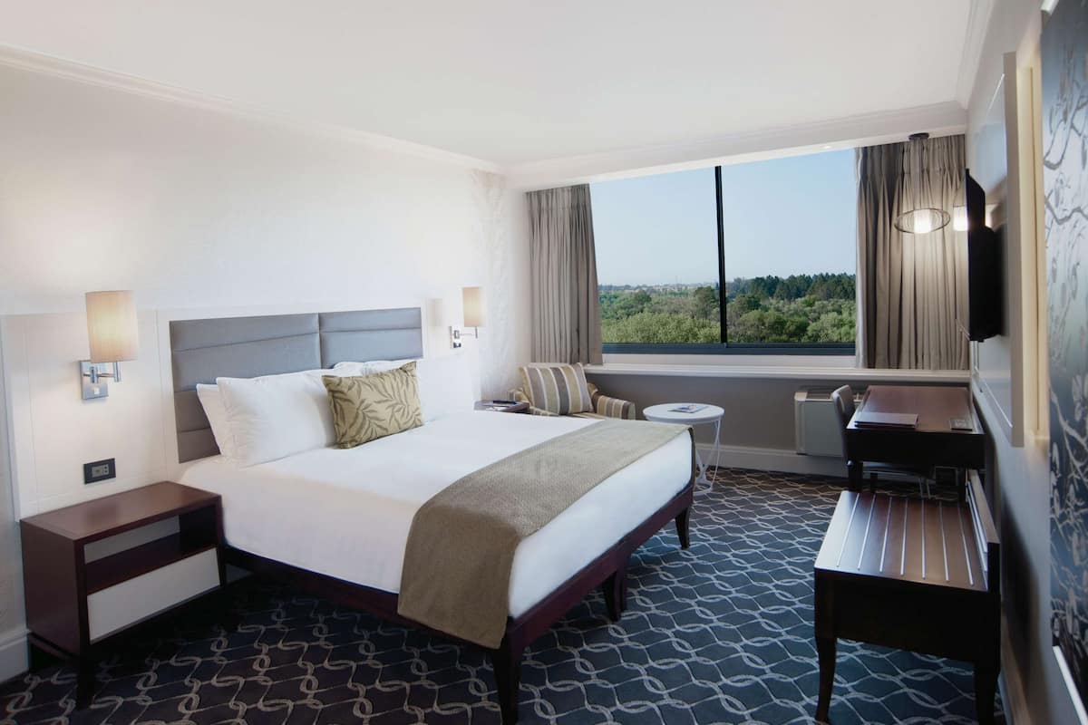 A hotel room with a large bed, bedside tables, a desk, a chair, and a view of the outdoors.