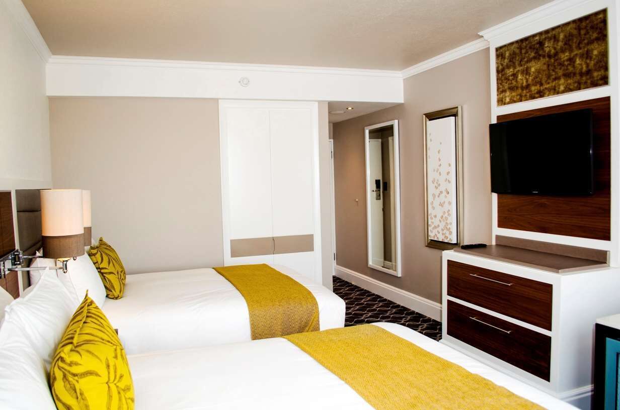 A hotel room with two beds, a TV, a mirror, and a wardrobe.