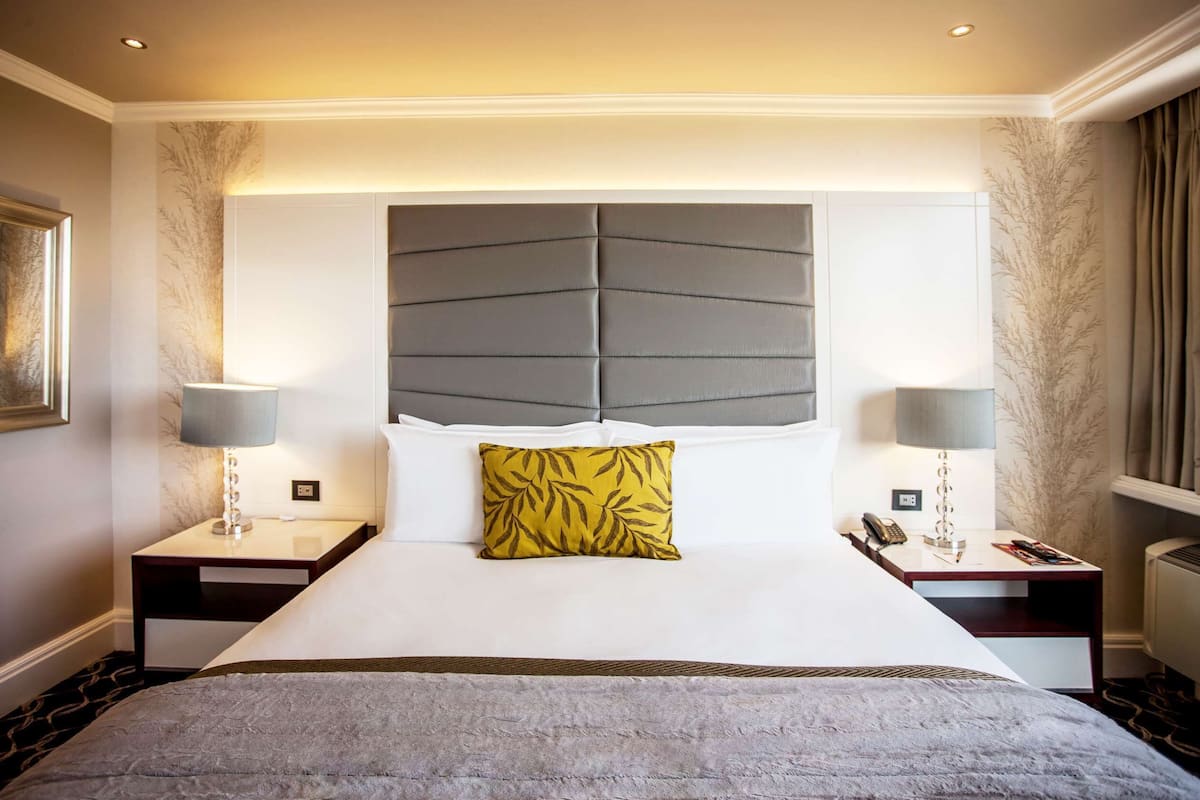A hotel room with a large bed, two bedside tables, a mirror, and a headboard with a leaf pattern.