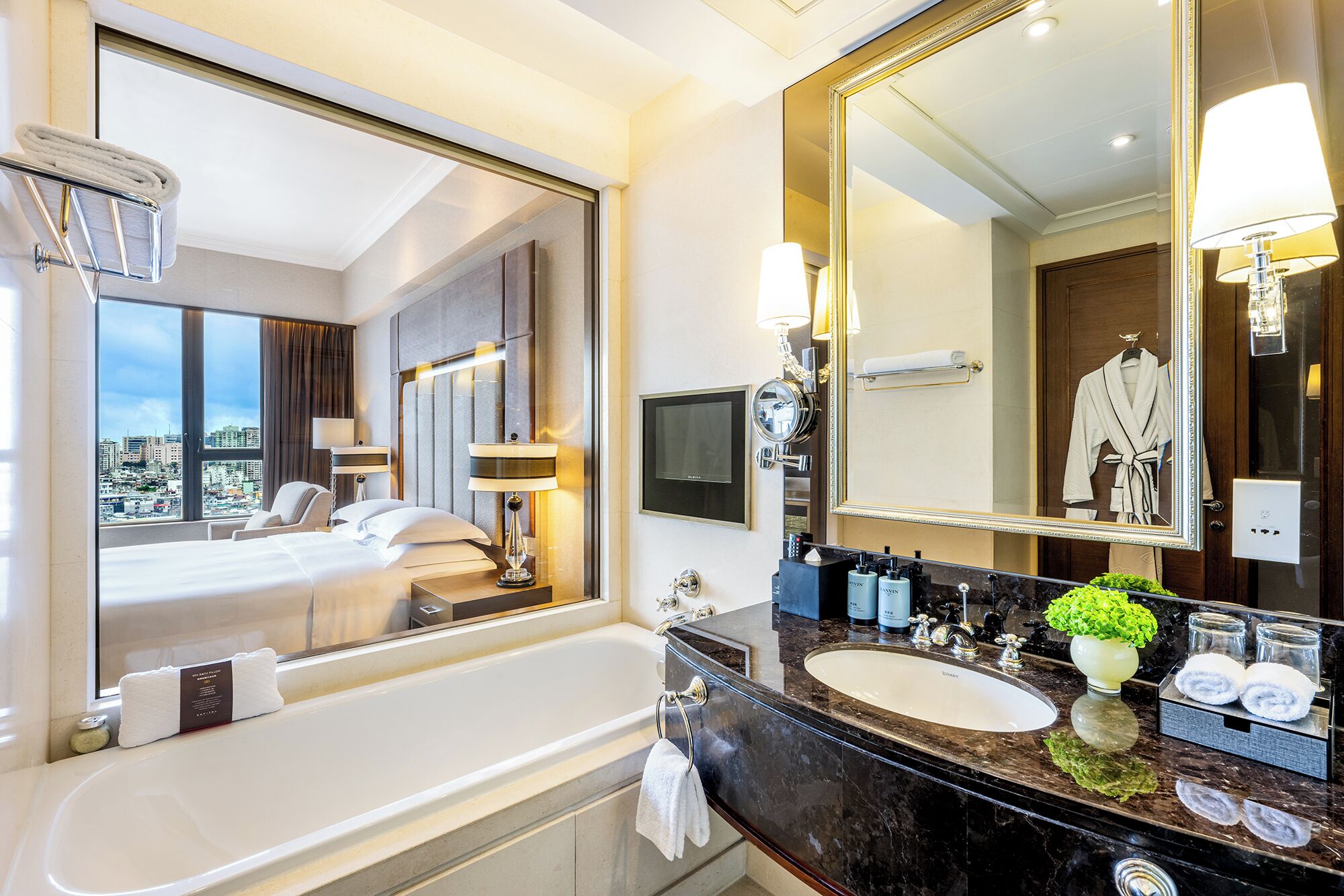 A hotel bathroom with a large mirror, a bathtub, a sink, and a city view.