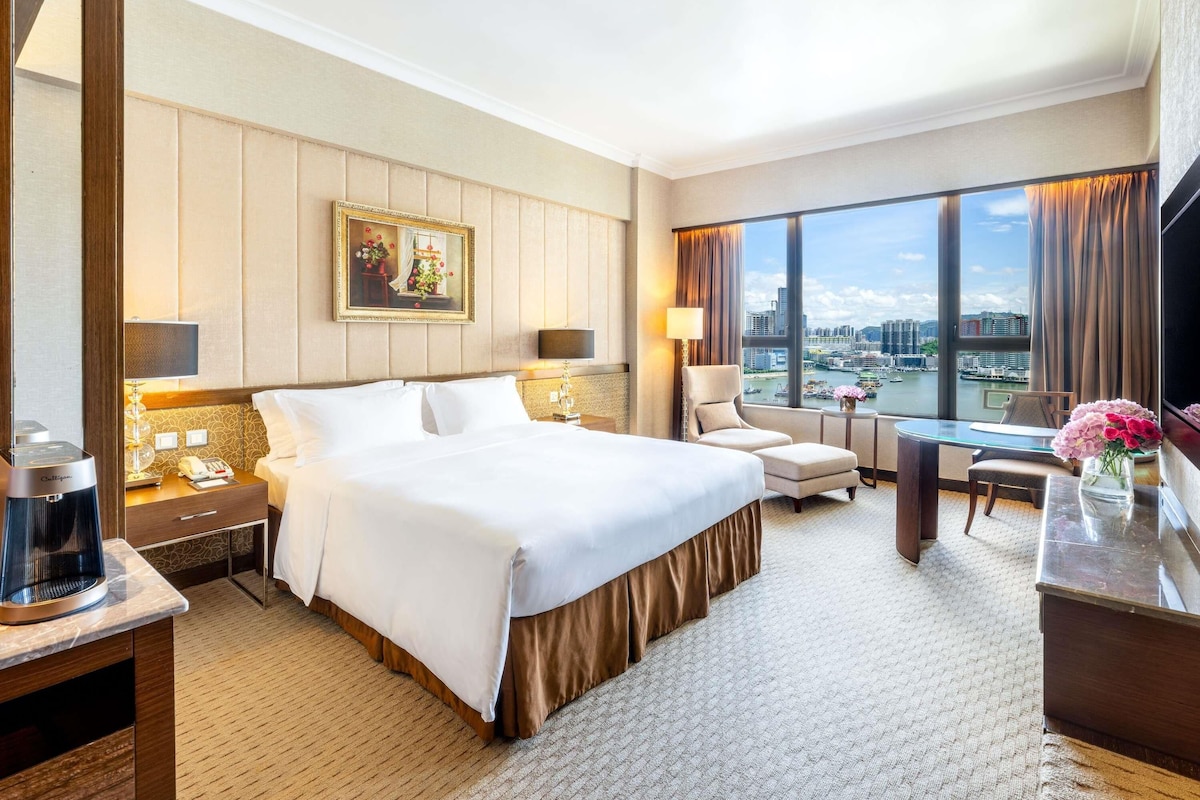 Camera d'albergo con un letto grande, una scrivania, una sedia, una televisione e vista sulla città.