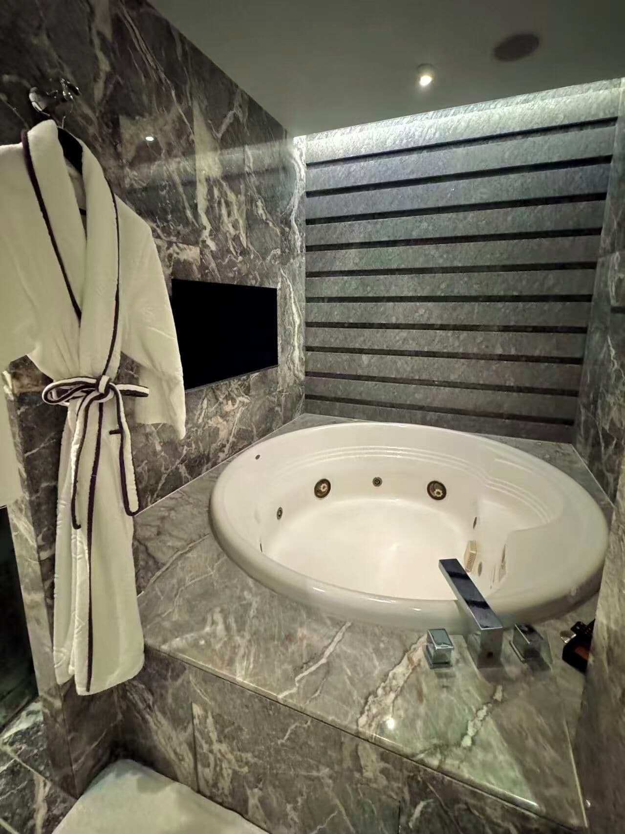 A modern bathroom with a marble floor, a freestanding bathtub, and a robe hanging on a hook.