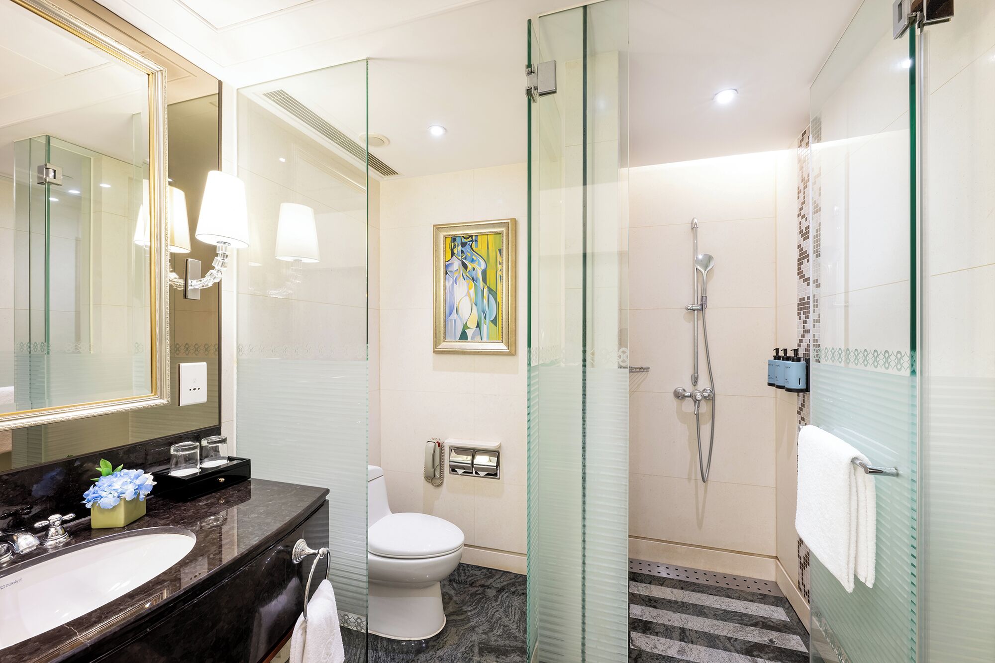 A modern bathroom with a glass-enclosed shower, a white toilet, and a marble sink.