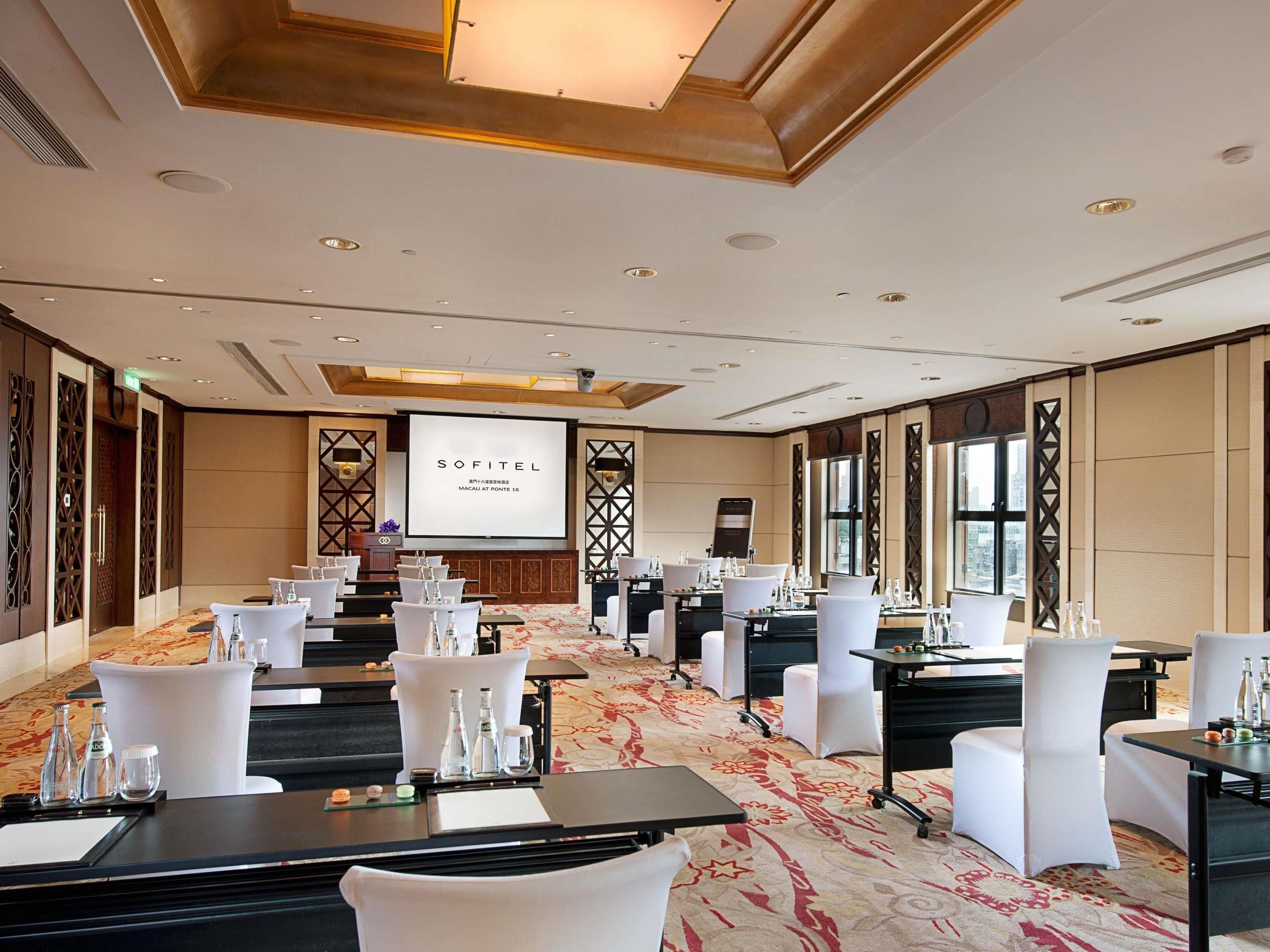 A conference room with tables, chairs, a projector screen, and a carpeted floor.