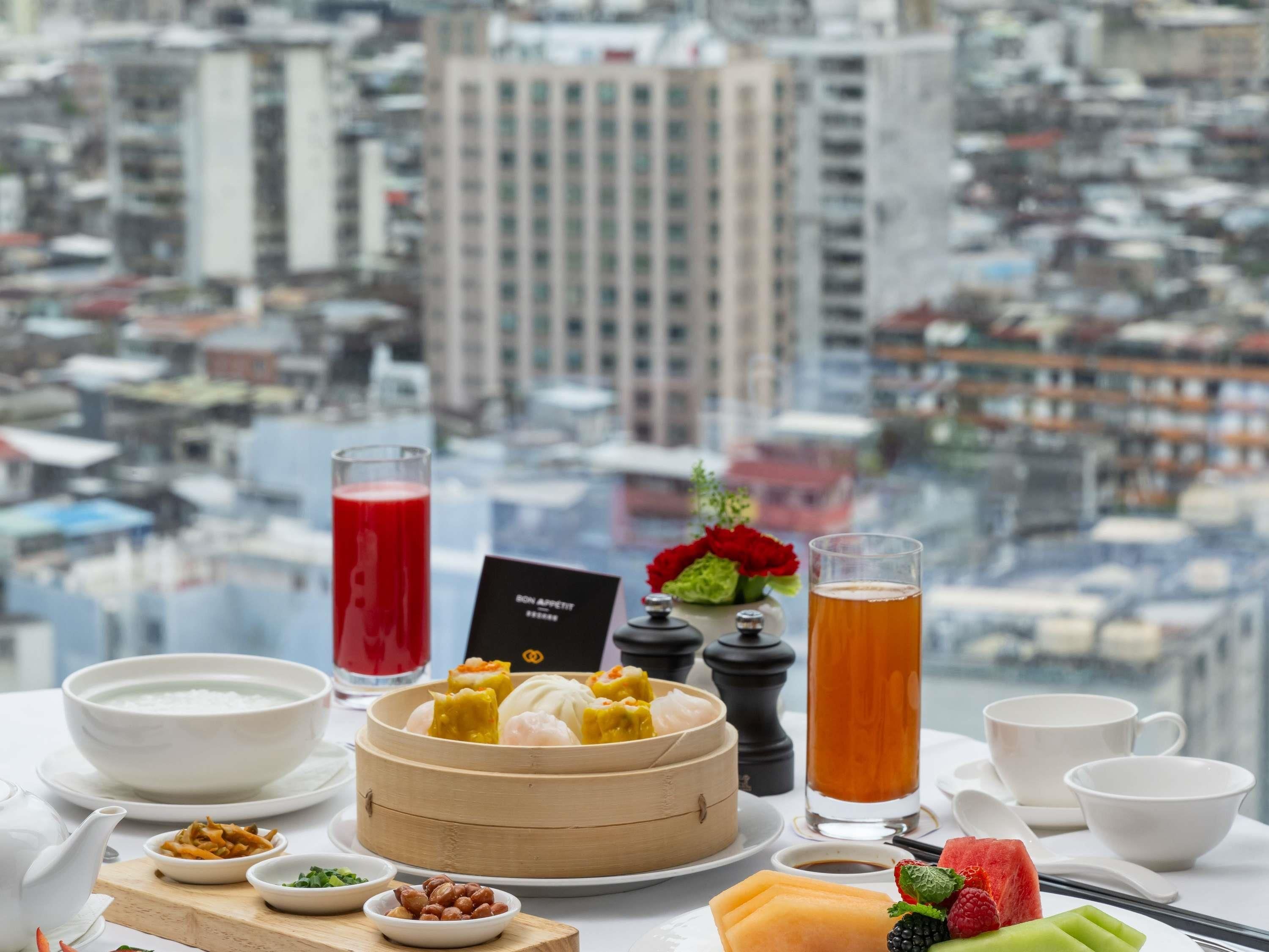 Una mesa con diversos platos, incluyendo dumplings, un tazón de sopa y una fuente de fruta, con vista a un paisaje urbano.