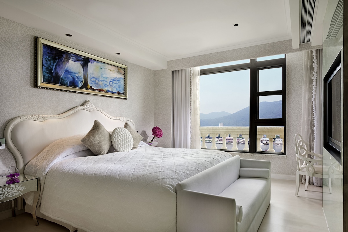 A bedroom with a large bed, a view of the sea, and a painting on the wall.