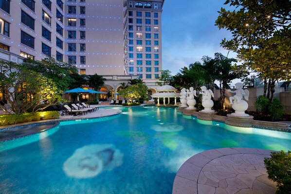 A hotel pool area with lounge chairs, a fountain, and a large building in the background. - Sofitel Macau At Ponte 16 (Macau)