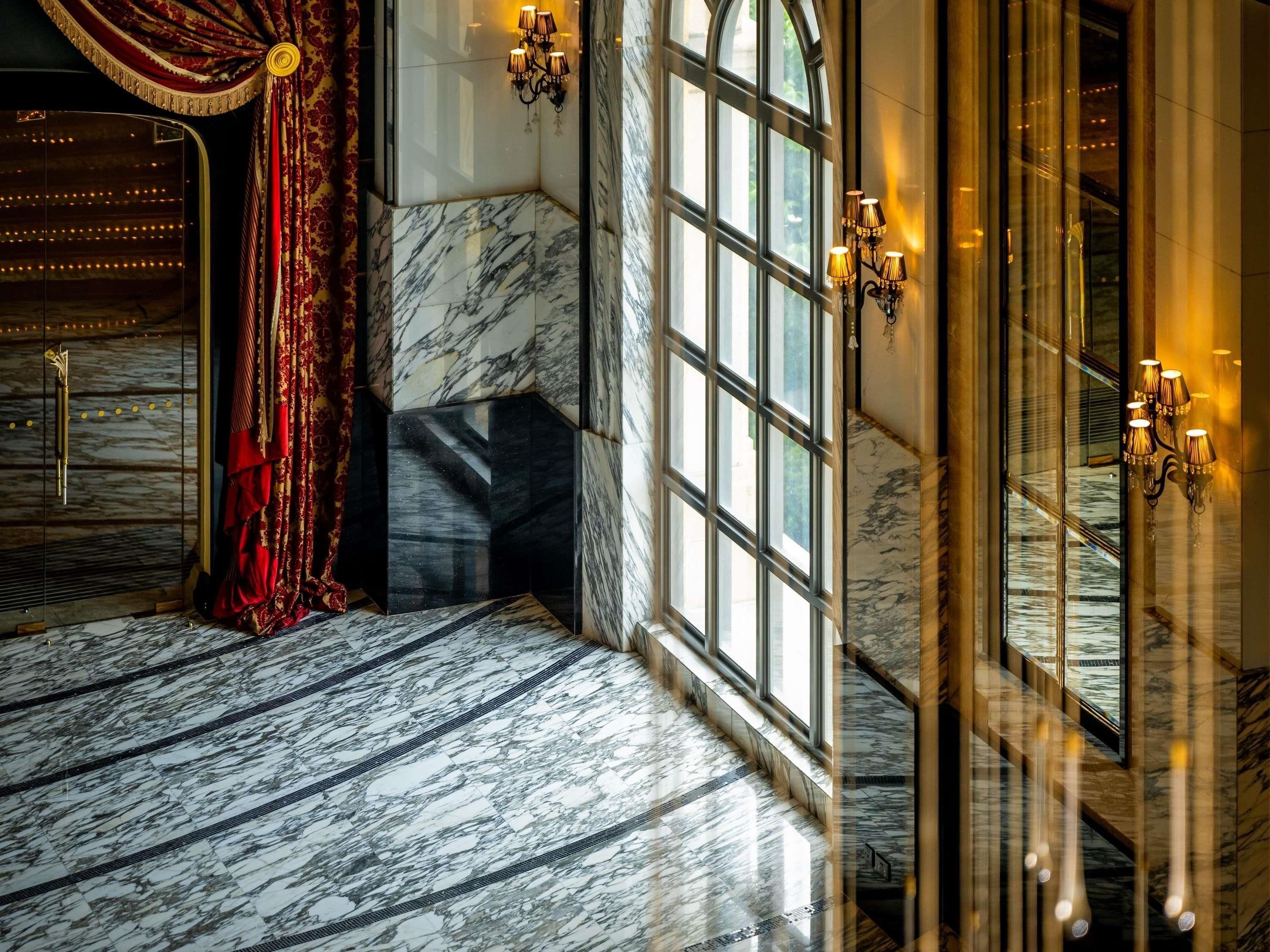 A luxurious hotel lobby with marble flooring, large windows, and elegant wall sconces.