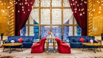 Eine luxuriöse Lobby mit zwei Sofas, einem zentralen Tisch und einem großen Fenster mit Vorhängen.