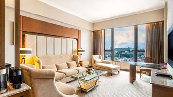 A hotel room with a sofa, armchair, coffee table, and a desk with a TV.