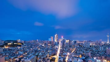 Un paisaje urbano al atardecer con imponentes rascacielos, una torre con un campanario característico y una torre con cables de suspensión.