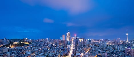 A cityscape at dusk with prominent high-rise buildings, a tower with a distinctive spire, and a cable-stayed tower.