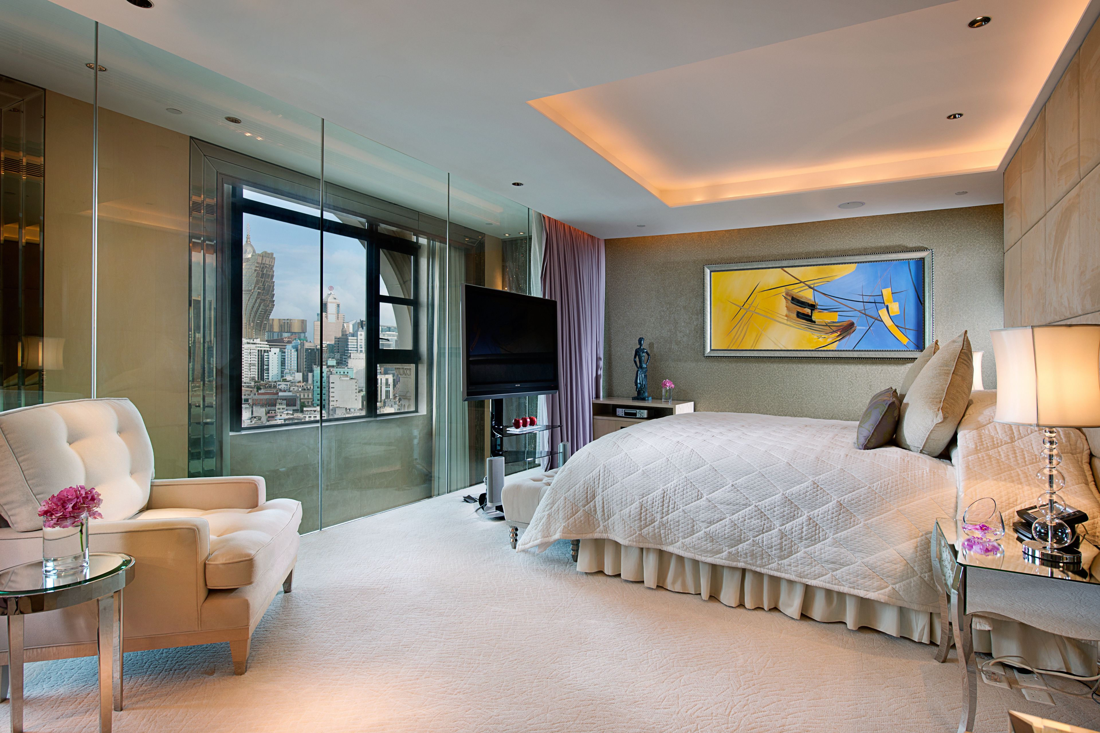 Quarto de hotel moderno com uma cama grande, divisória de vidro, televisão de tela plana e vista para a cidade.