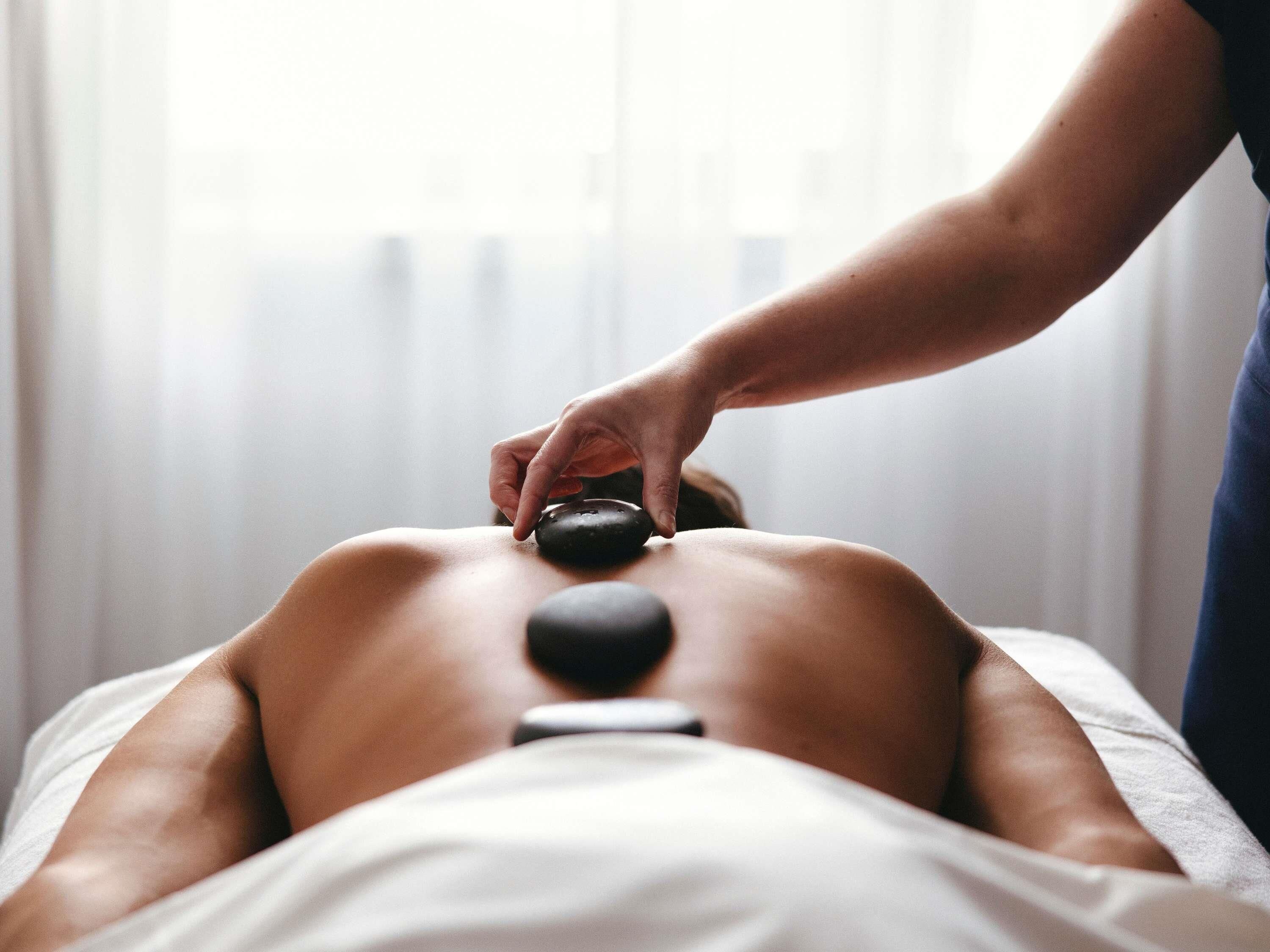 A person receiving a back massage with a stone on their back.