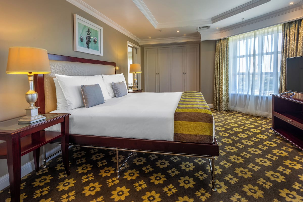A hotel room with a large bed, two bedside tables with lamps, a TV, and a window with curtains.