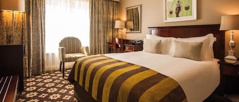 Habitación de hotel con una cama grande, una silla, un escritorio y una lámpara.
