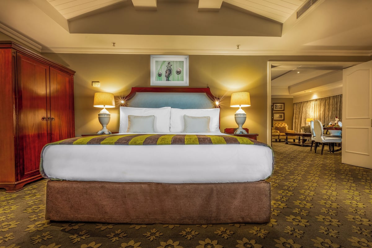 A large bed with a colorful blanket, two bedside lamps, a framed picture above the bed, and a wooden wardrobe.