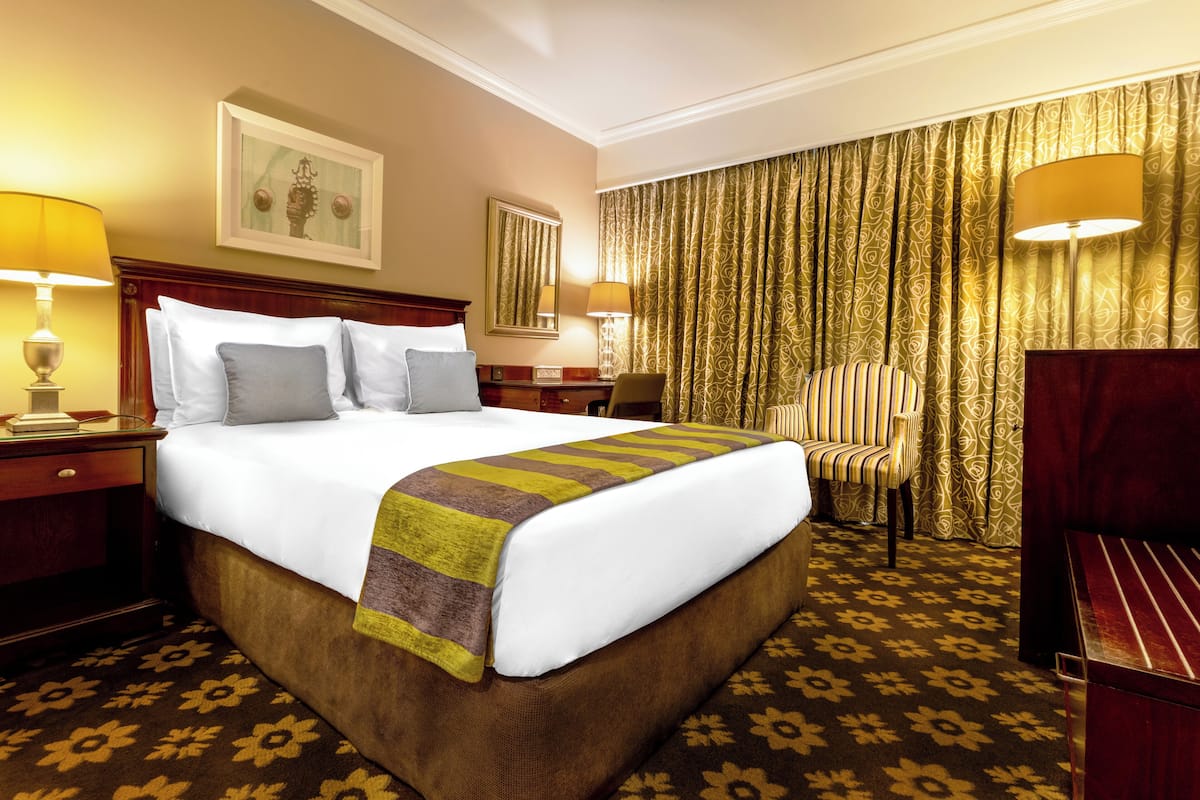 A hotel room with a large bed, two bedside tables, a chair, a desk, and a large window with curtains.