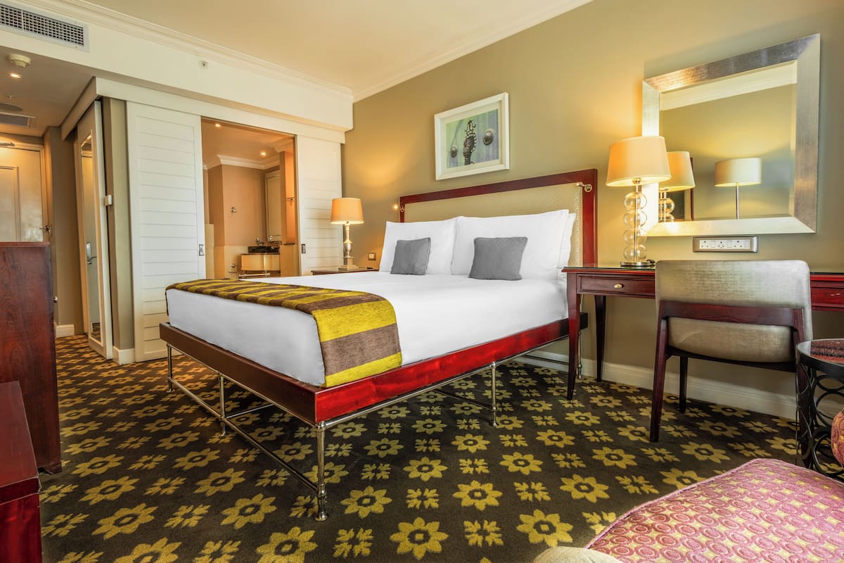 A hotel room with a bed, bedside tables, a chair, a desk, and a mirror.