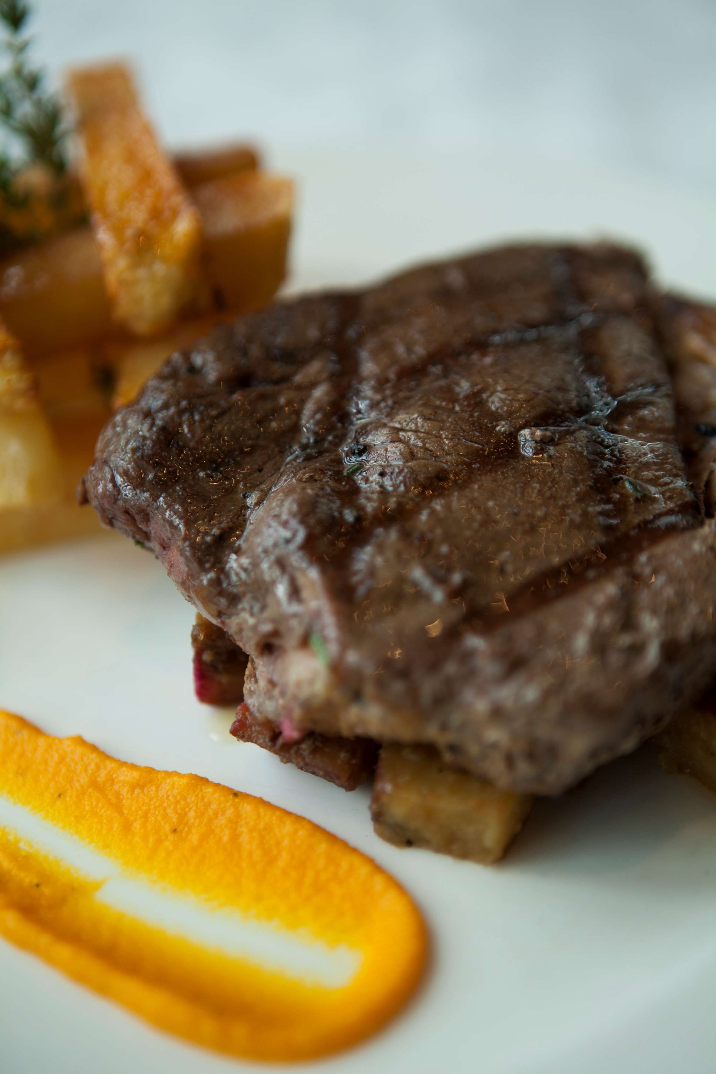 A steak with potatoes and a slice of orange on a plate.