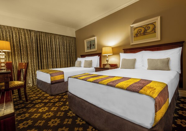 A hotel room with two beds, a desk, and a chair.