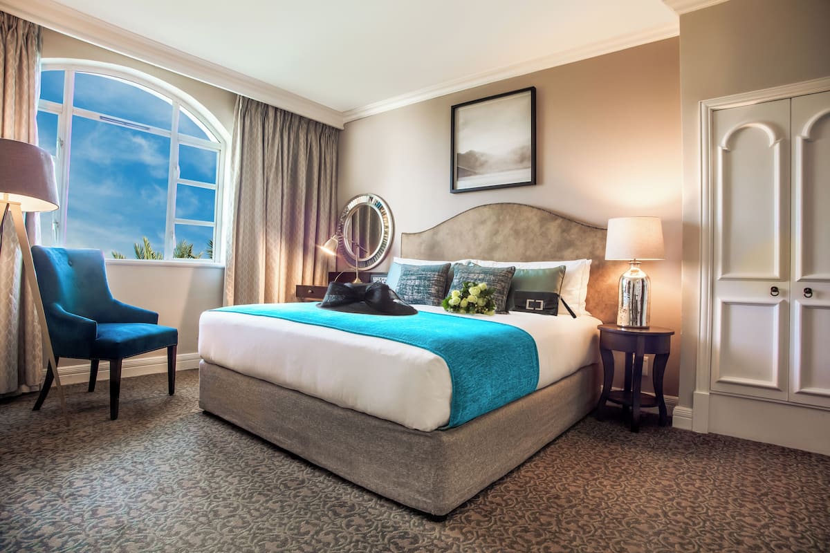 A hotel room with a large bed, a chair, a bedside table with a lamp, a mirror, and a door.