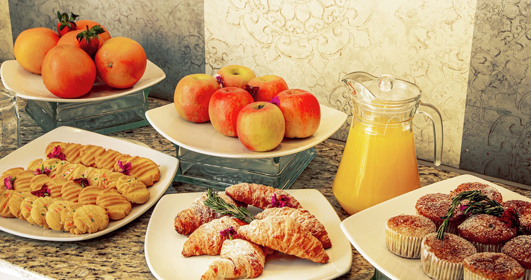 A breakfast buffet with fruits, pastries, and a pitcher of juice.