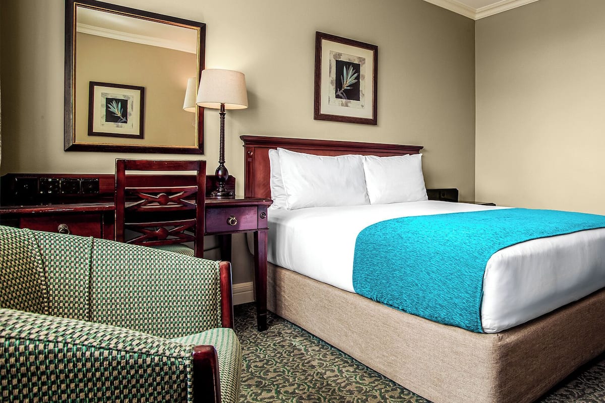 A hotel room with a bed, a desk, a chair, and a lamp.