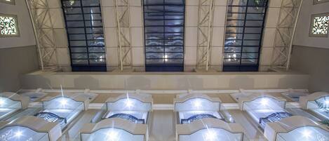 Eine Hotelhalle mit mehreren reihenweise angeordneten Betten, großen Fenstern mit dekorierter Glasverkleidung und einem modernen architektonischen Design.
