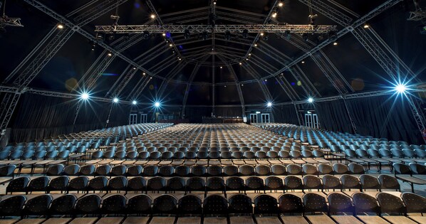 An indoor auditorium with rows of seats, a stage with lighting equipment, and a balcony area.