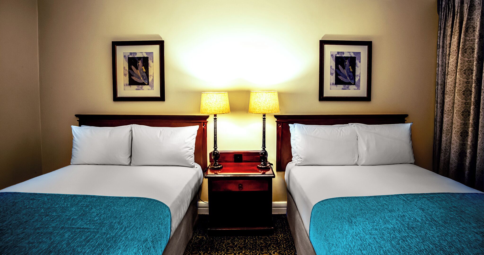 Een hotelkamer met twee enkele bedden, een nachtkastje met lampen en lijstwerken aan de muren.