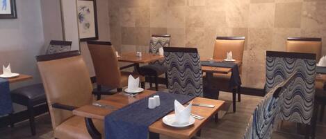 A restaurant with tables and chairs, some with blue and black patterned cushions.