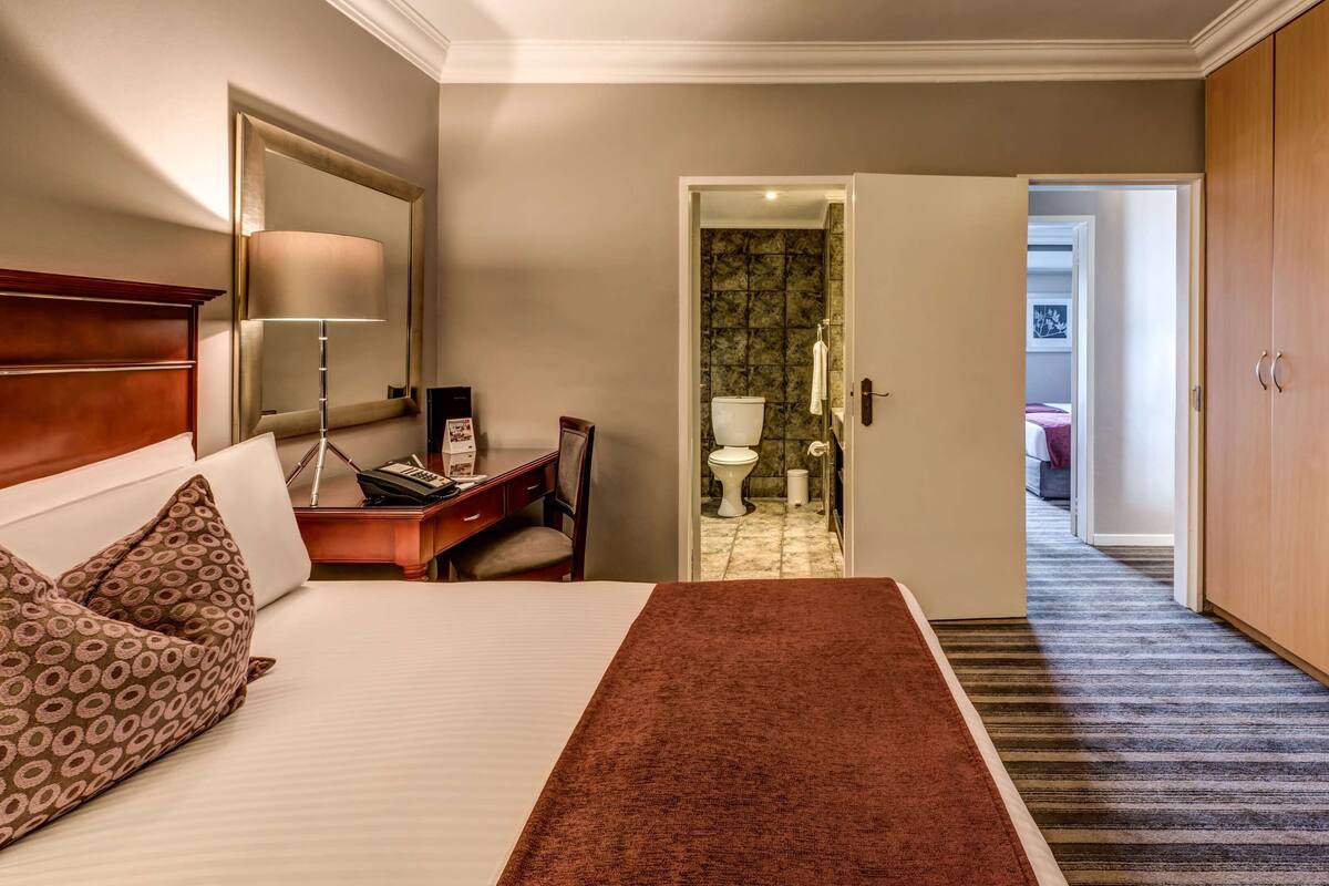 Ein Hotelzimmer mit Bett, Schreibtisch, Stuhl und einem durchgegangenen Tür sichtbaren Badezimmer.