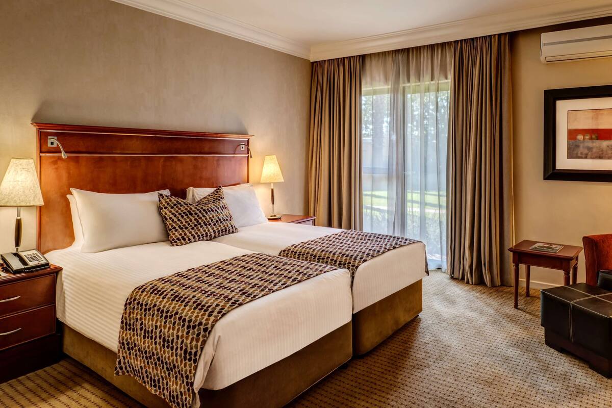 Ein Hotelzimmer mit zwei Betten, einem Schreibtisch, einem Stuhl, einem kleinen Tisch und einem gerahmten Bild an der Wand.