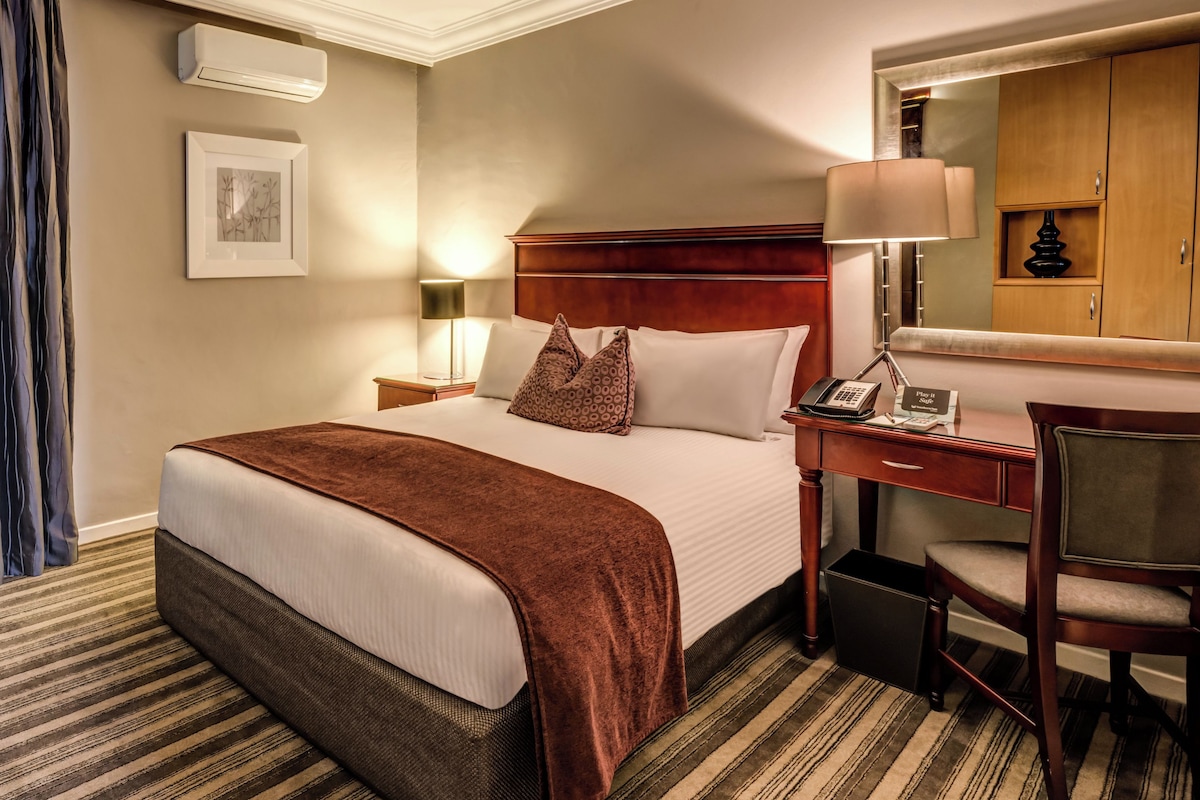 Une chambre d’hôtel avec un grand lit, un bureau avec un téléphone, une chaise, une lampe et un tableau au mur.