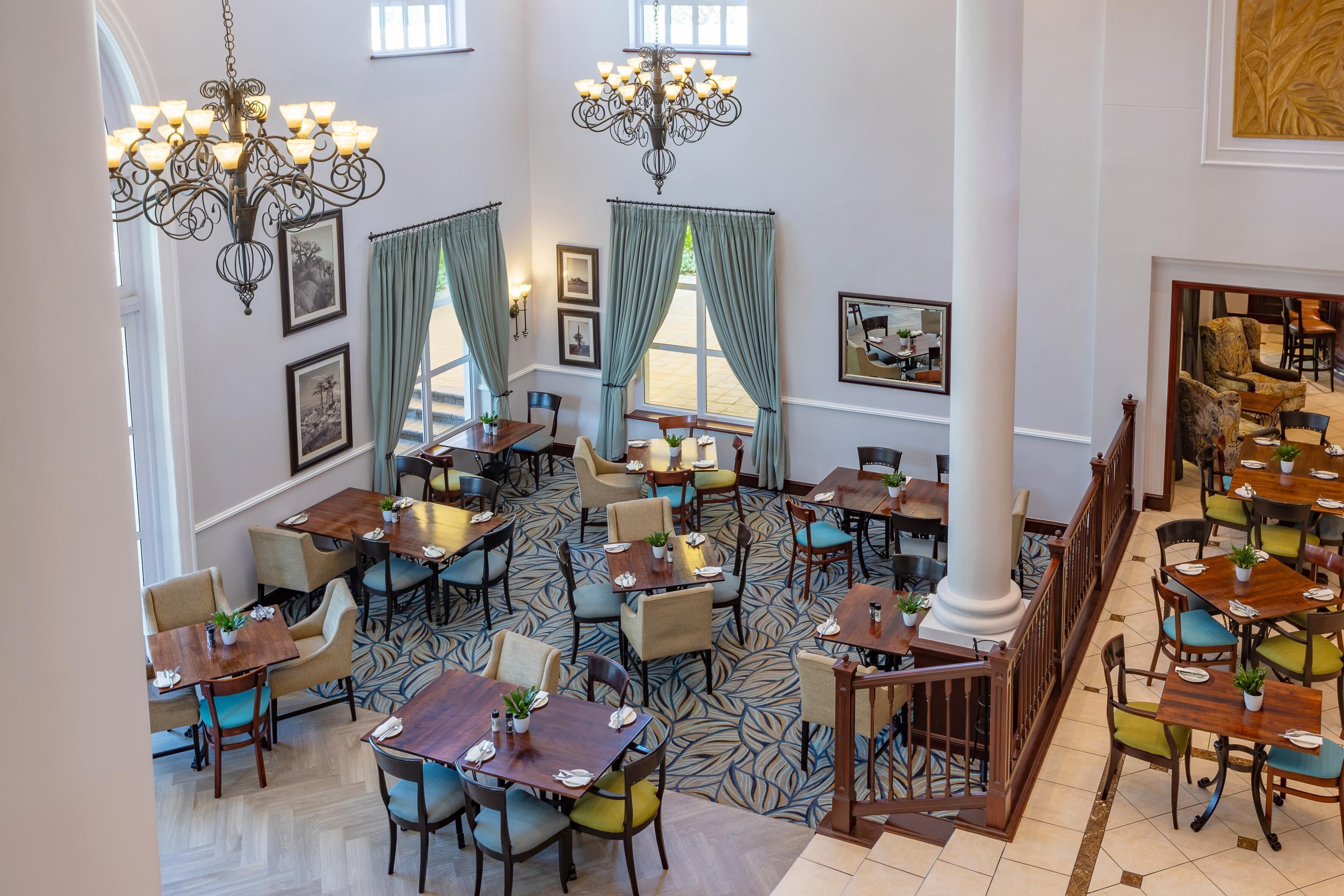 A spacious hotel lobby with multiple dining areas, large chandeliers, and a patterned floor.