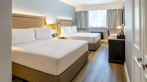 A hotel room with two beds, a desk, a chair, a lamp, and a window with curtains. - Southern Sun Mbombela (Mbombela)
